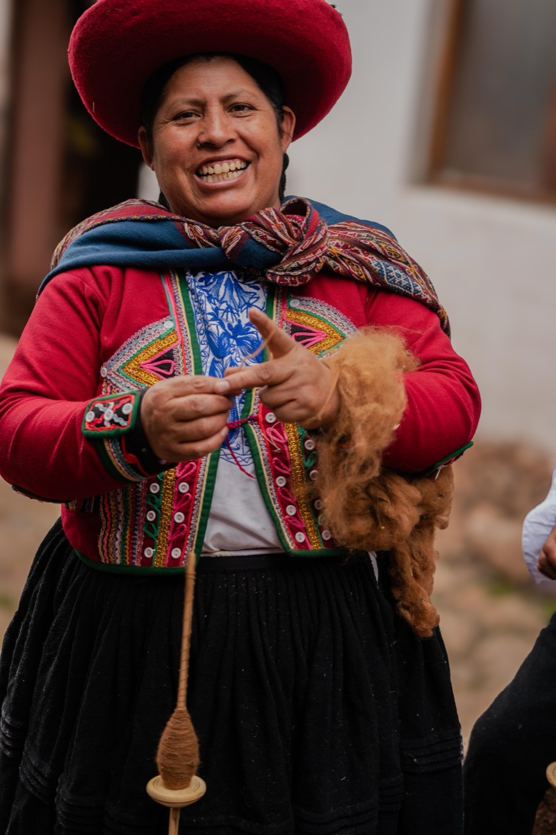 Augusta Pumacahua Pumayali smiling while spinning wool with a drop spindle in traditional Chinchero dress, Cusco, Peru