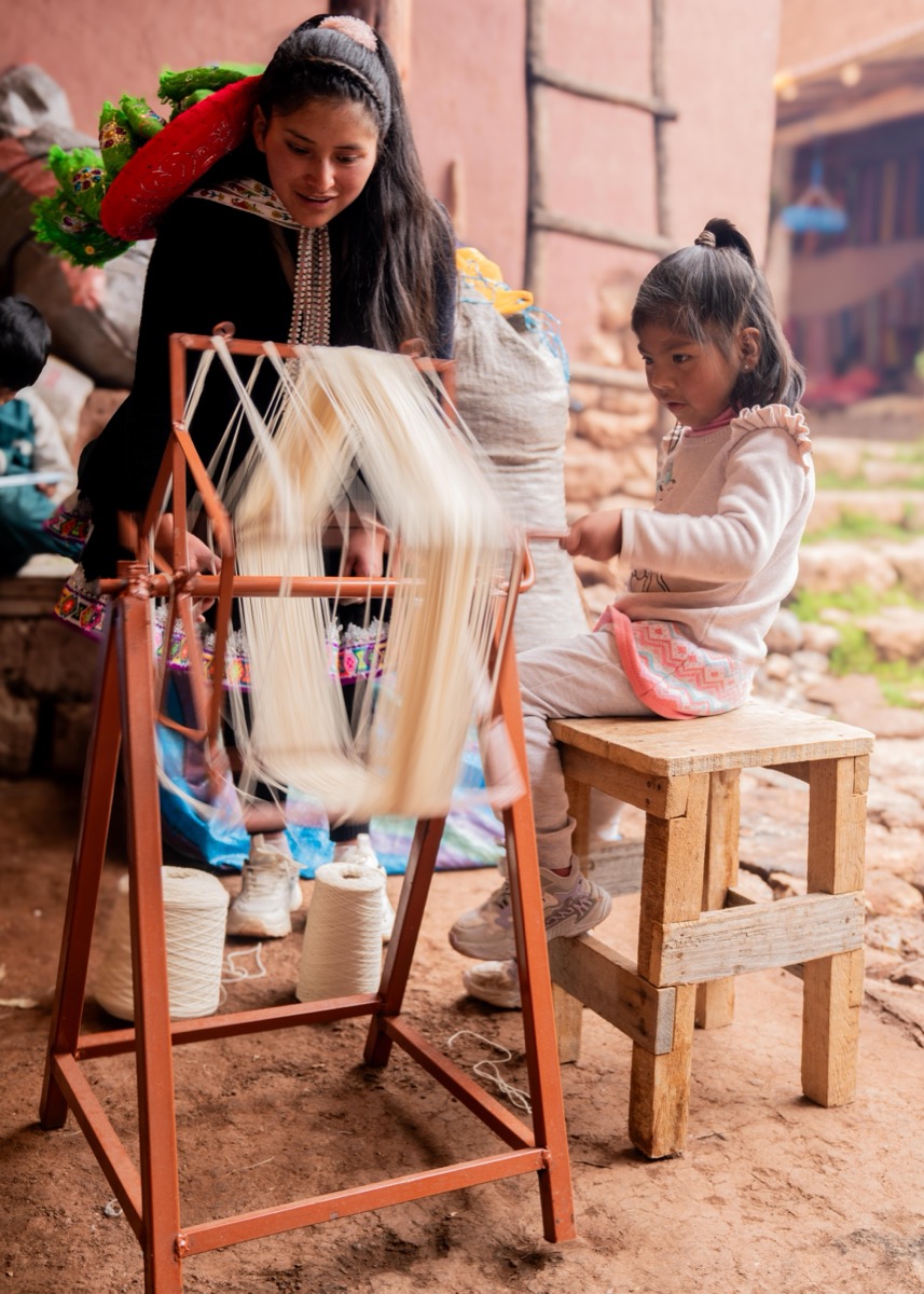 Older girl in traditional Chinchero dress showing a young child how to use a warping frame, Cusco, Peru