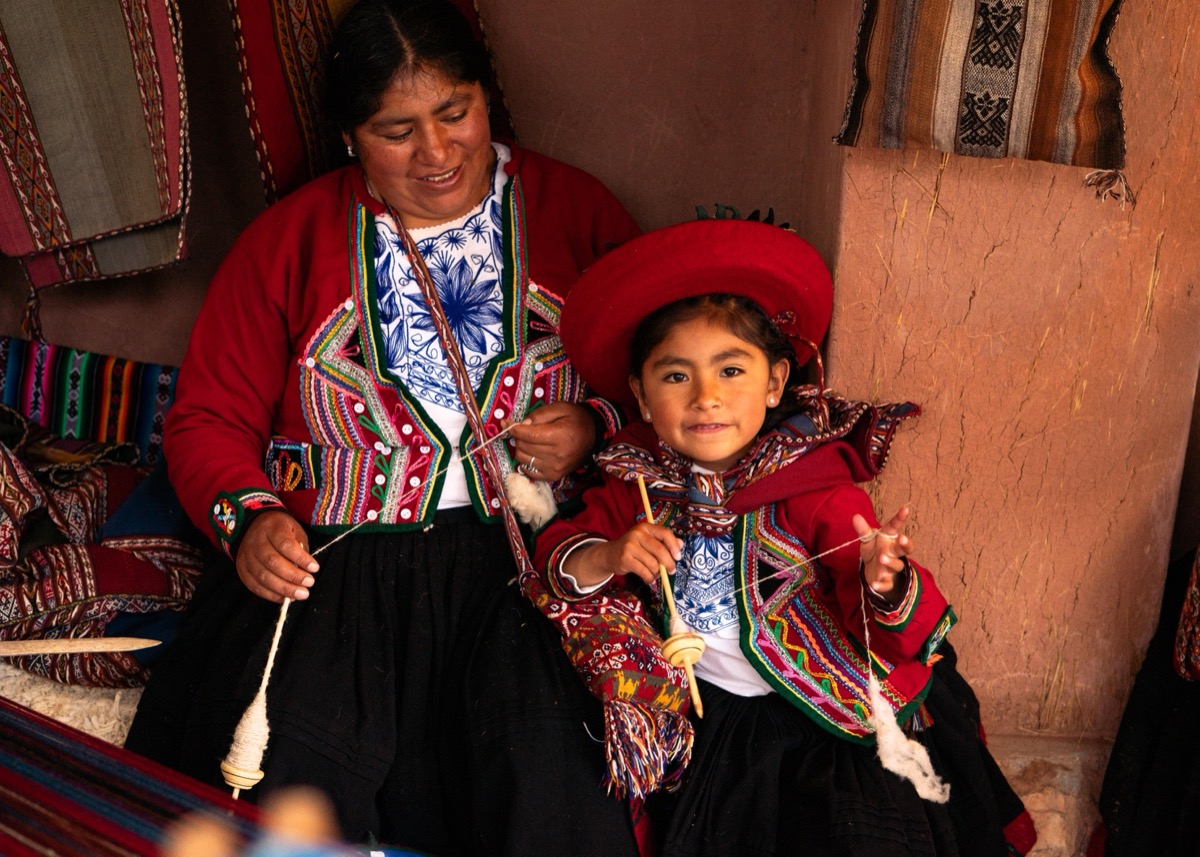 Woman and young girl in traditional Chinchero dress spinning wool together with drop spindles in a weaving studio, Cusco, Peru