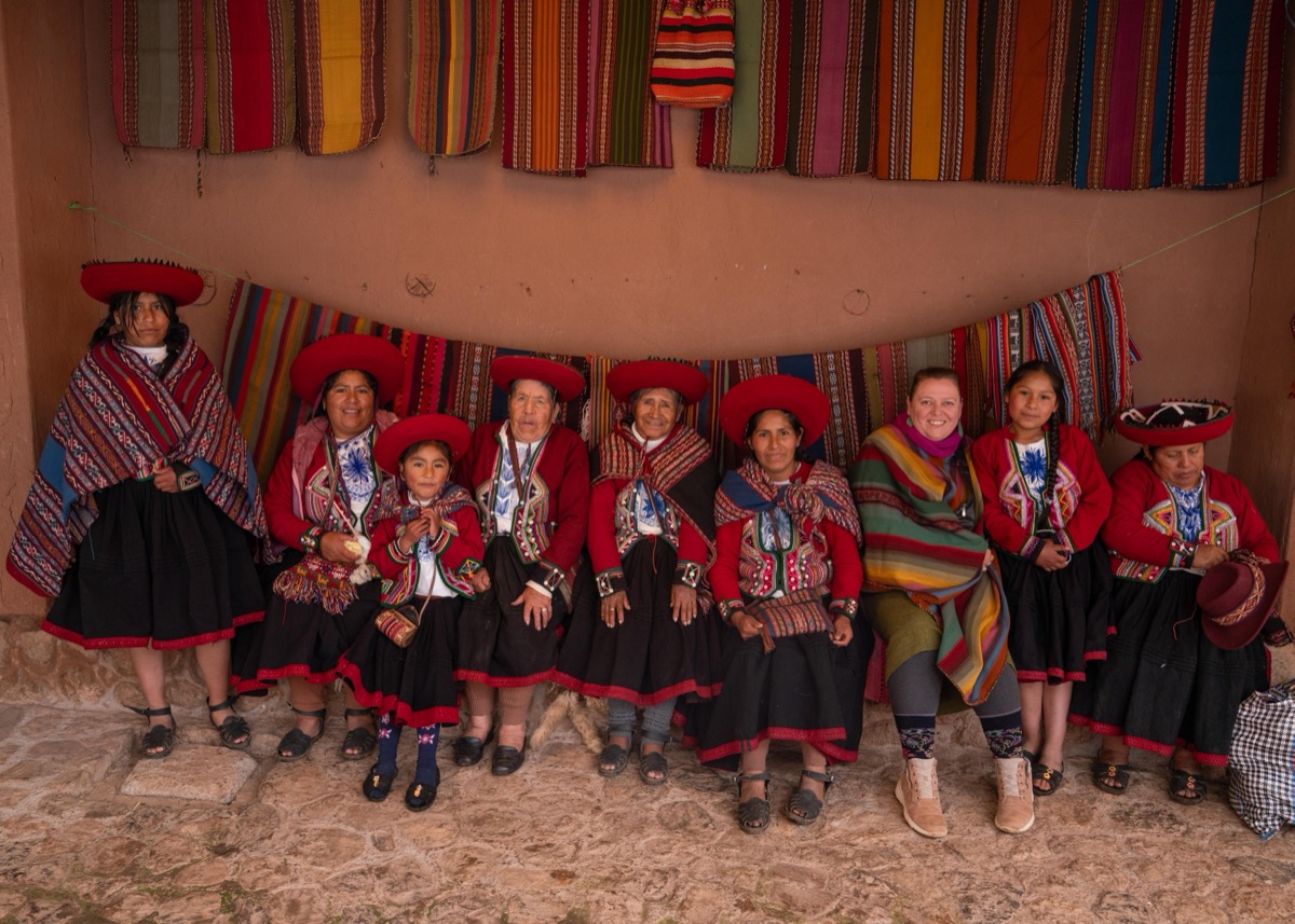 Group of Colores de Abundancia artisan weavers in traditional Chinchero dress seated in front of colorful handwoven textiles, Cusco, Peru