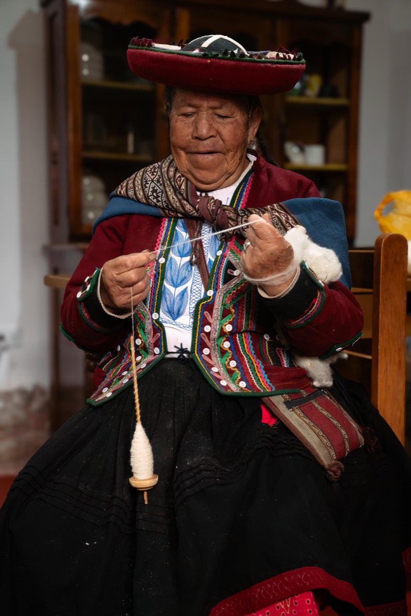 An elder weaver in traditional Chinchero dress spinning wool with a drop spindle, Cusco, Peru