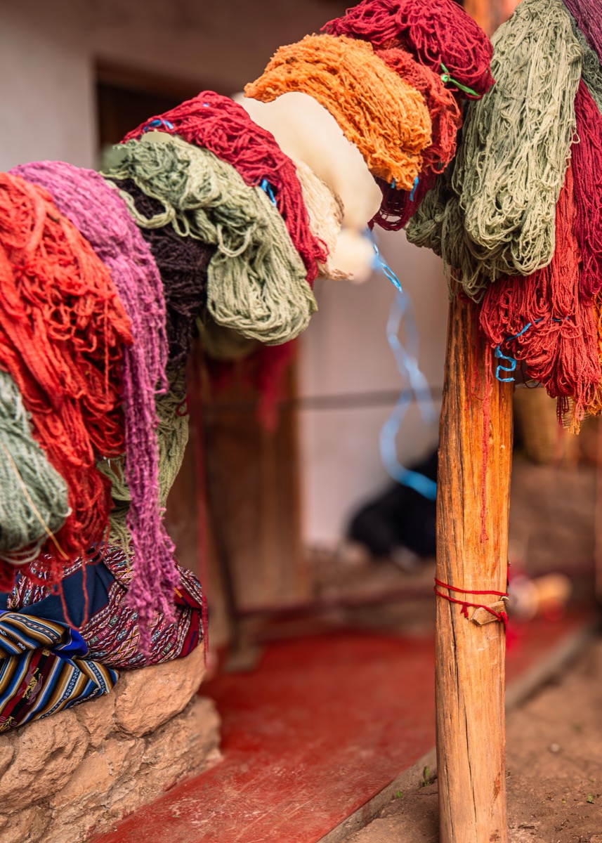 Naturally plant-dyed yarn in vibrant colors hanging to dry on a wooden post at a Colores de Abundancia workshop, Chinchero, Peru