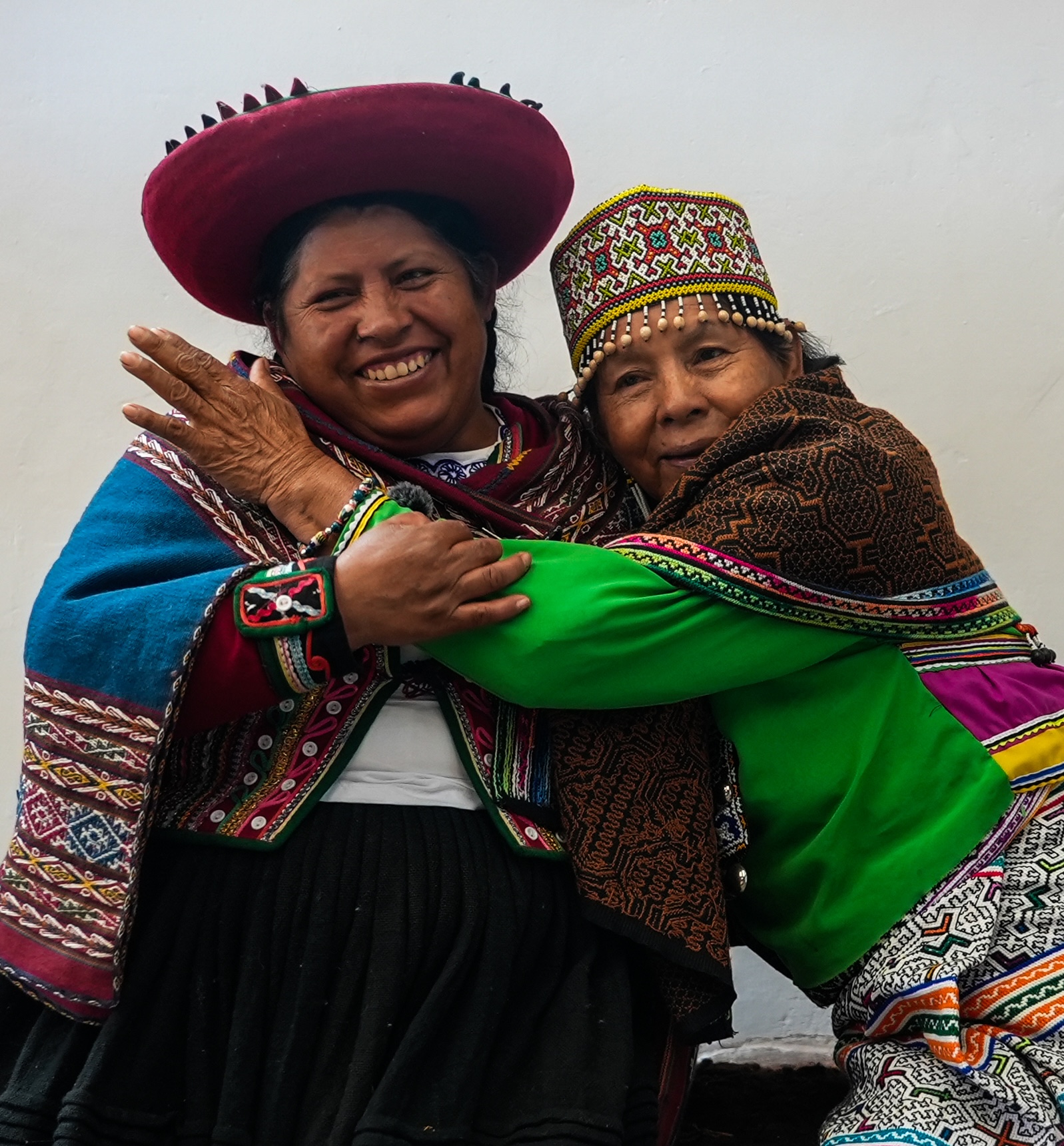 Two women in traditional Andean and Amazonian dress embracing and smiling, Peru