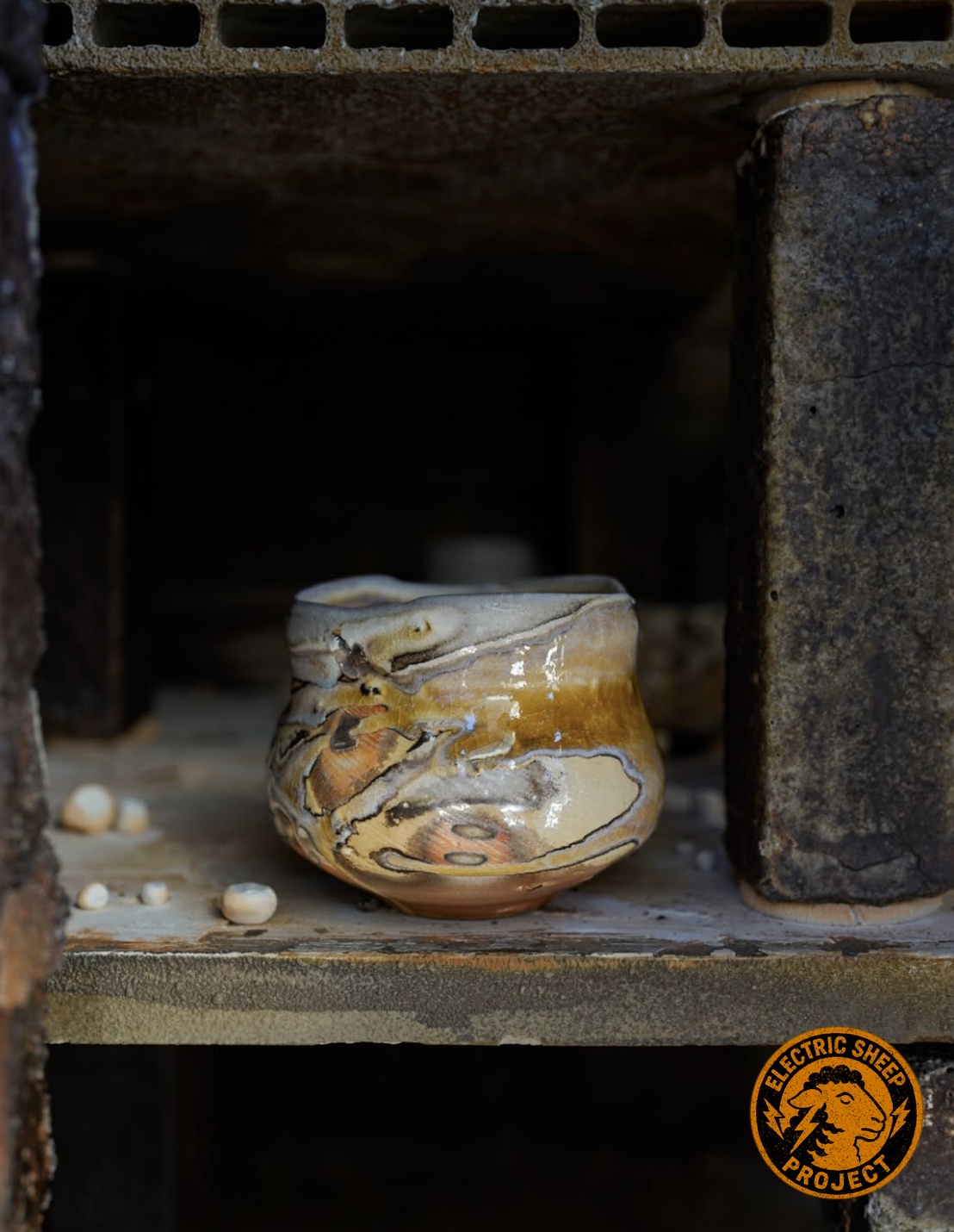 Handmade ceramic bowl with flowing amber and earth-toned glaze resting inside a kiln at the Electric Sheep Project studio