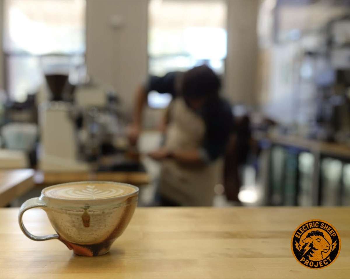 Handmade ceramic coffee cup with latte art on a wooden counter at the Electric Sheep Project