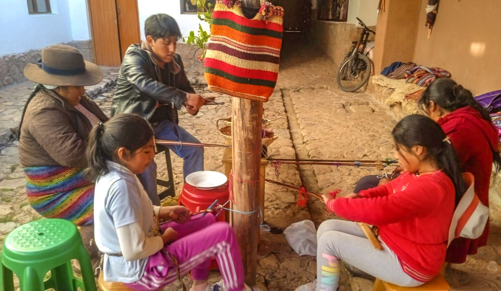 Augusta Pumacahua, Robert Singona, and students weaving together at looms in a Chinchero courtyard