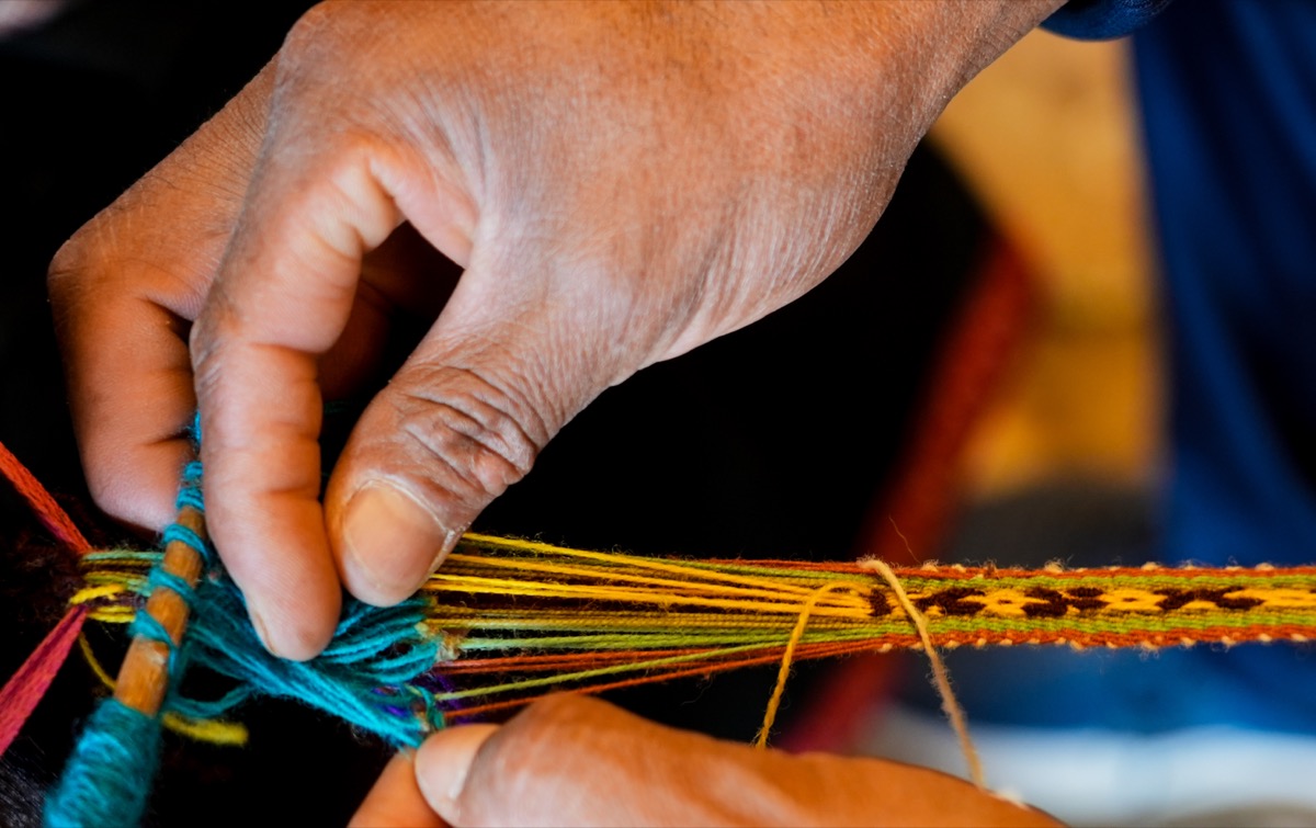 Close-up of hands weaving colorful threads on a jakima loom, Chinchero, Peru