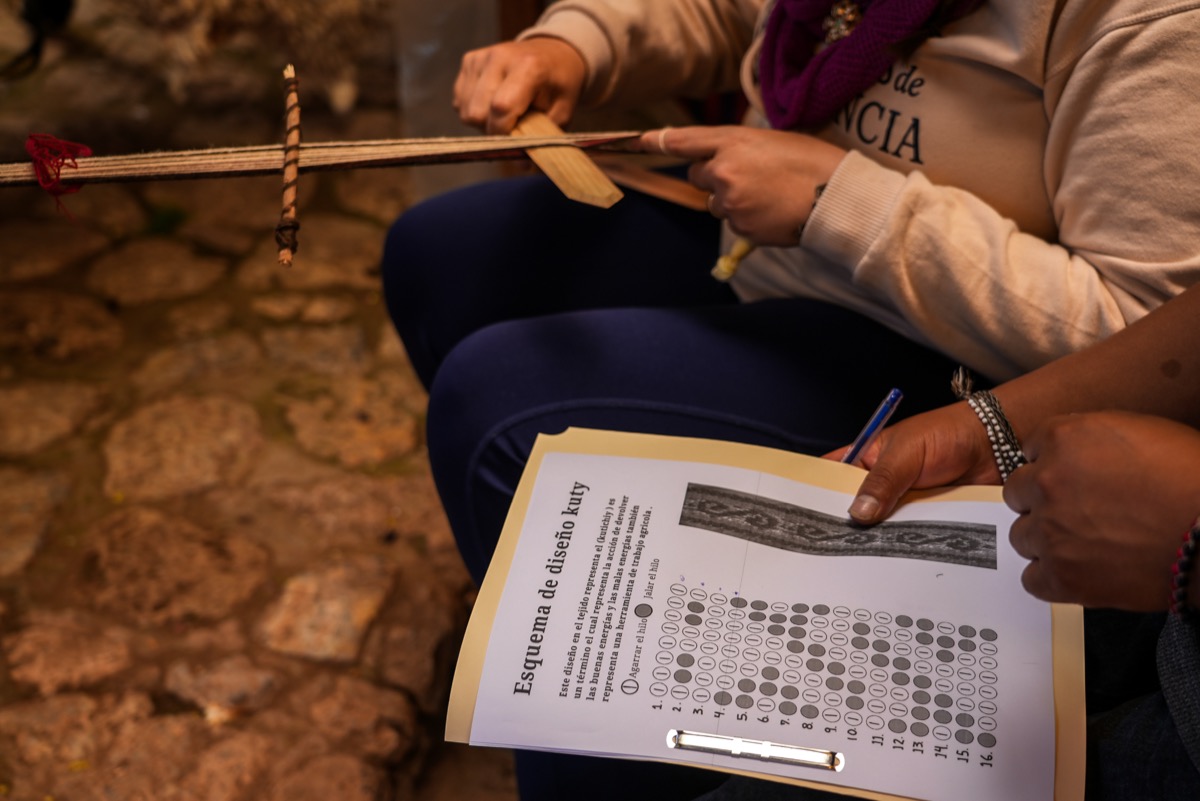 A student following the Kuty design schematic while weaving a jakima at a Colores de Abundancia class, Chinchero, Peru